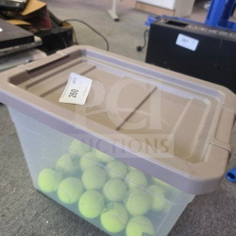 Lot of tennis balls in a clear plastic storage bin with taupe lid. Bin labeled with auction tag "220". Balls appear gently used.