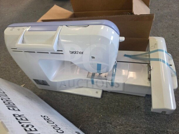 Brother embroidery machine with white body, blue accents, and visible tape. Includes a box labeled "Polyester Embroidery Colors."