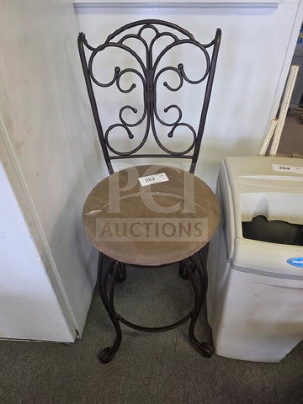 Ornate metal stool with curved backrest, brown cushioned seat, and label "203." Elegant scrollwork design, in good condition.