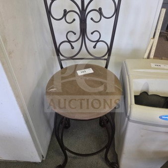 Ornate metal stool with curved backrest, brown cushioned seat, and label "203." Elegant scrollwork design, in good condition.