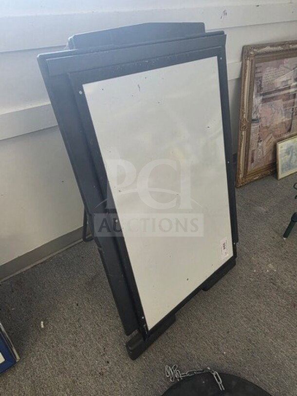 Black-framed standing dry erase board, rectangular, lightly used, suitable for signs or messages.