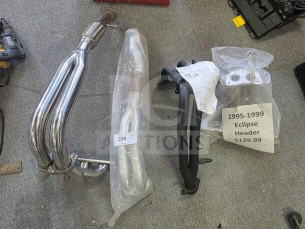 Lot of miscellaneous exhaust headers, including chrome and black metal models. One labeled "1995-1999 Eclipse Header $129.99."