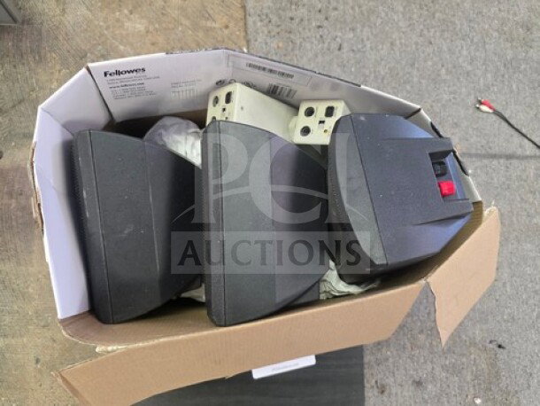 Box of miscellaneous electronics including black speakers and power strips, assorted brands. Condition appears used.