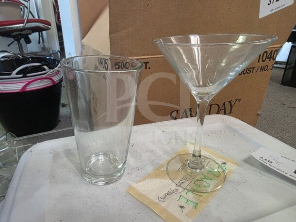 Lot of miscellaneous glasses, including a tall pint glass with measurement markings and a martini glass. Appears in good condition.
