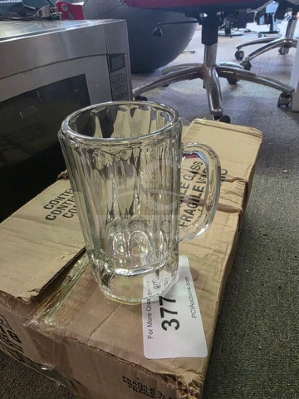 14oz glass mug, clear ribbed design, excellent condition, sitting on cardboard box with visible lot number tag, industrial setting.