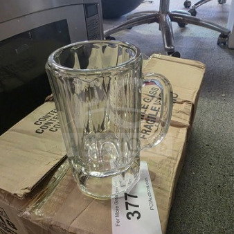 14oz glass mug, clear ribbed design, excellent condition, sitting on cardboard box with visible lot number tag, industrial setting.