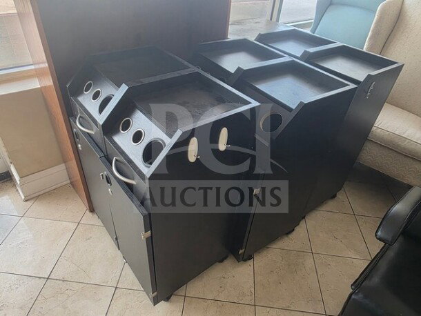 Lot of 4 black salon trollies with pull-out sections and handle grips. Each features tool slots and storage compartments. Good condition.