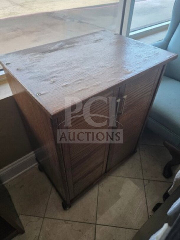 Wooden cabinet with two doors, metal handles, and a smooth top. Light wear visible, compact size suitable for small spaces.