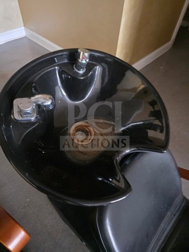 Black shampoo chair backwash unit with integrated sink, featuring silver faucet. Visible wear with rust around drain.
