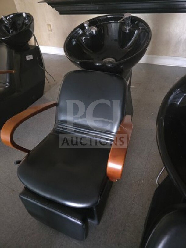 Shampoo chair backwash unit with black upholstery, wooden armrests, and integrated basin. Good condition.