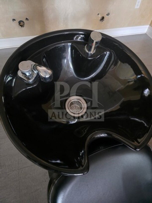 Black shampoo chair backwash unit with basin, faucet, and drain. Features ergonomic design and durable material.