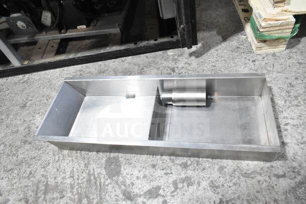 Stainless steel part on industrial floor, likely a component for commercial kitchen equipment.