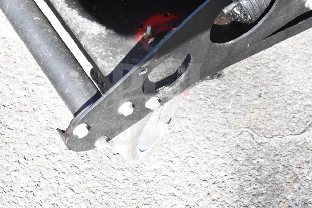 Close-up of a Briggs & Stratton Vanguard XTP120 Generator frame on pavement, showing bolts and wheel attachment.