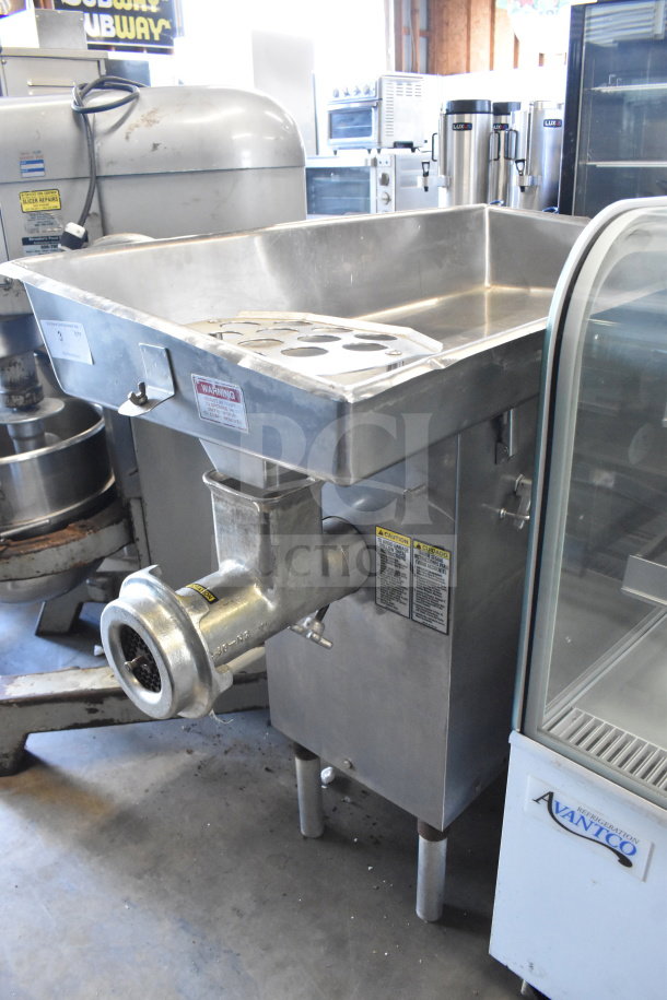 Commercial floor-style meat grinder, stainless steel, large tray, used condition. Safety and operation warning labels visible.