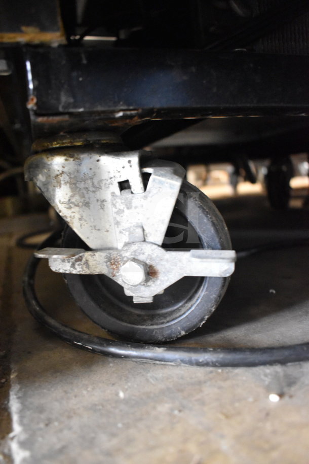 True GDM-472F-HC Freezer caster wheel detail, showing a sturdy metal bracket and rubber tire on concrete floor.