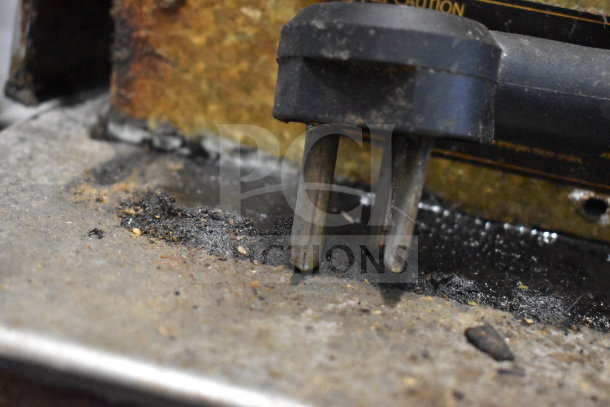 Close-up of a three-prong plug against a worn metal surface, showing grime and use, possibly part of the Turbochef NGC oven setup.