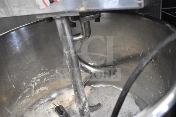 Commercial spiral dough mixer with bowl, guard, and dough hook attachment; shows some flour residue indicating use.