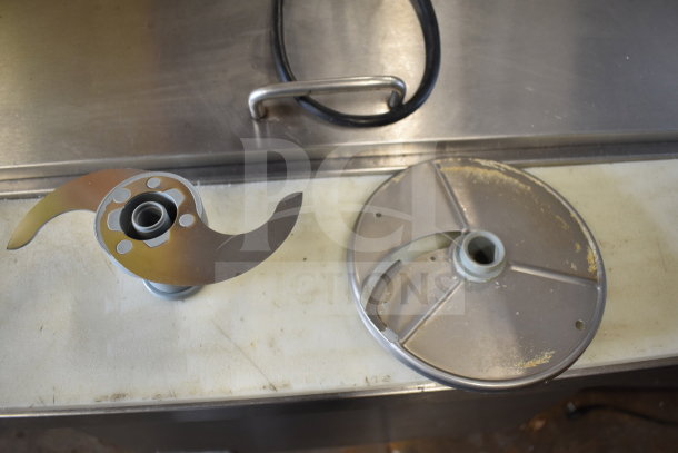Robot Coupe R2 food processor blades on countertop; includes sharp S-shaped and flat disc blades, in used condition.