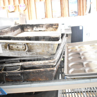 Seven assorted baking items including metal roasting pans and two bun baking pans, in used condition, with auction label.