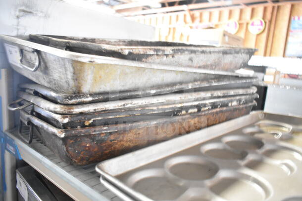Stack of 7 metal roasting and bun baking pans, used condition, varied sizes, perfect for bulk cooking needs.