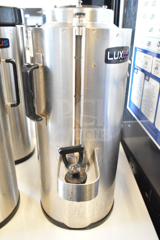 Two Fetco TPD-15 Luxus beverage dispensers, stainless steel, black handles, visible Luxus branding, good condition.