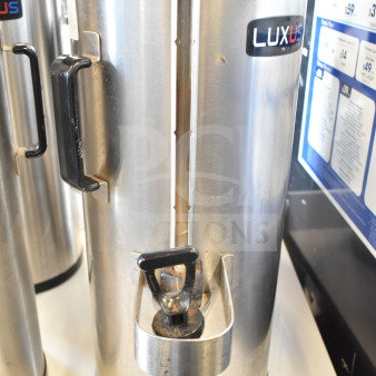 Two Fetco TPD-15 Luxus beverage dispensers, stainless steel, black handles, visible Luxus branding, good condition.