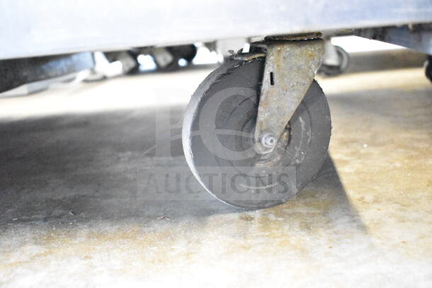 True TUC-48 undercounter cooler wheel. Black commercial caster, slightly worn, attached to rusted metal bracket. Suitable for mobility.
