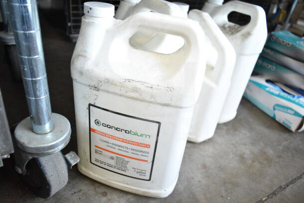 Concrobium Disinfectant 1-gallon jug, white, slightly worn, near boxes and casters. Part of a cleaning supply lot.