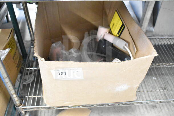 Cardboard box containing six items including hair dryers and brushes, all with cut power cords. Auction label visible.