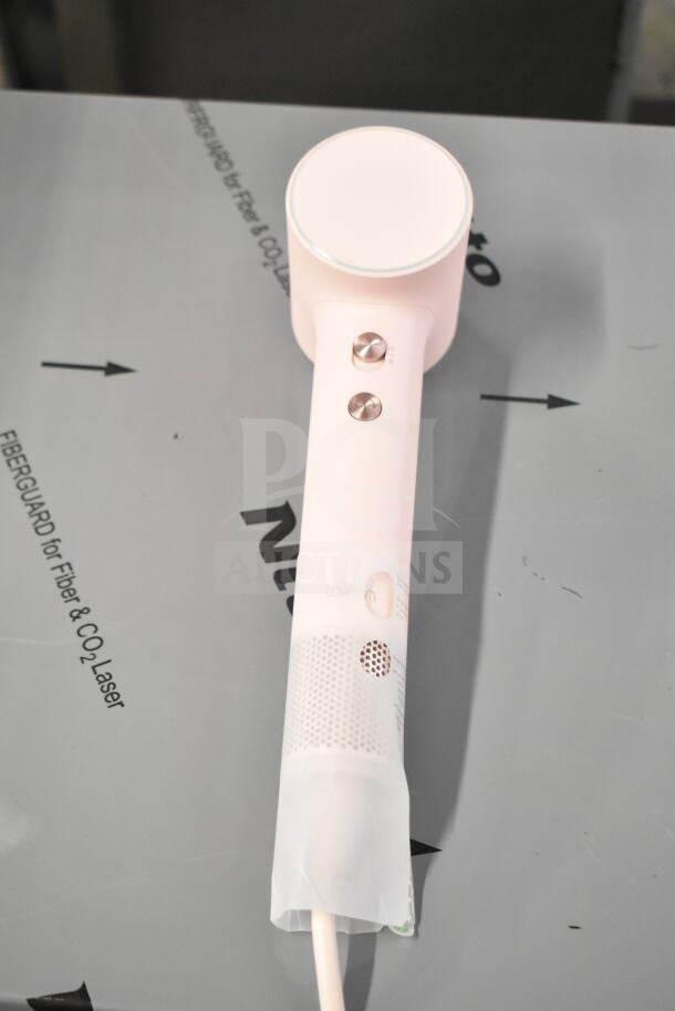Pink hair dryer with cut power cord, featuring metal control buttons and circular air vent design.