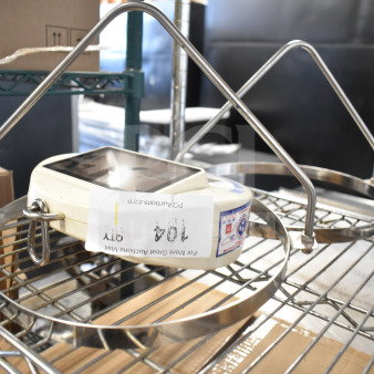 Detecto SCS30 hanging produce scale with two metal attachments, displayed on a metal shelf. Labels show item code and info.
