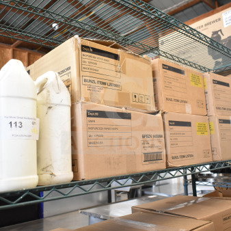 Boxes of Biopure BZK Wipes and various items on a metal shelf, labeled as new scratch and dent auction items.