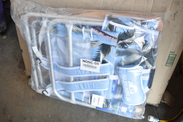 Foldable beach chair with blue palm design in packaging. Marked "SUN NINJA". New condition. Visible label "NONC-03".