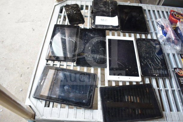 Various tablets on metal rack, mostly with cracked or dirty screens, indicating used condition. One visible label marked "182".