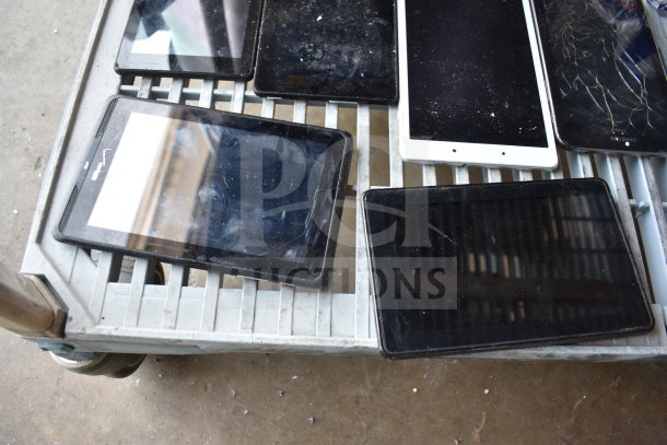 Nine assorted tablets with varying conditions, some with cracked screens, displayed on a metal shelf.