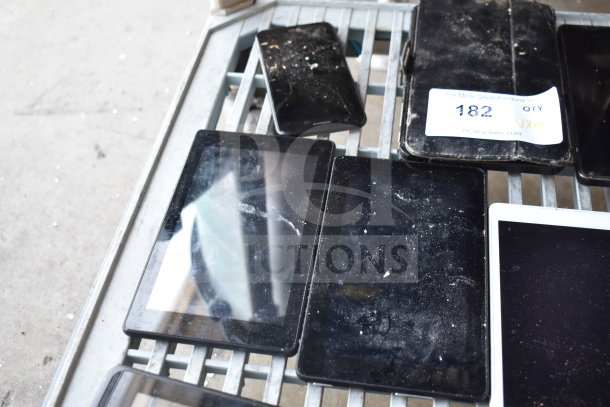 Nine assorted tablets on a metal shelf, varying in condition with visible dust and wear. Auction tag reads "QTY: 9."