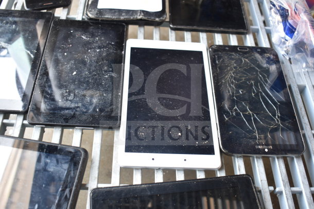 Nine mixed tablets on a shelf, varying conditions, including a cracked Samsung. Dust visible. Auction item: 9x bid value.