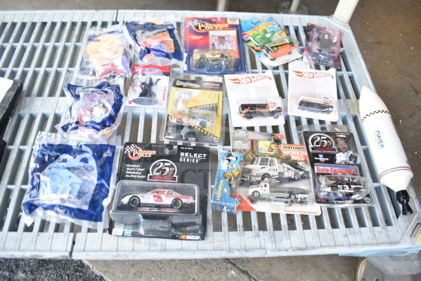 16 assorted collectible items including die-cast cars, Hot Wheels, and packaged toys, arranged on a table.