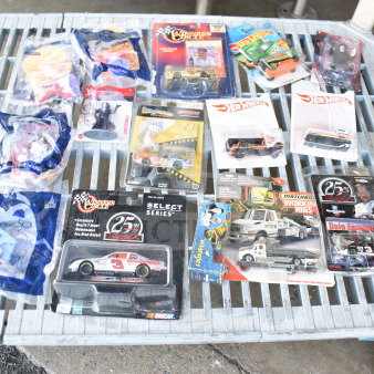 16 assorted collectible items including die-cast cars, Hot Wheels, and packaged toys, arranged on a table.