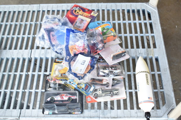 Assorted items including die-cast cats, Hot Wheels cars, and a NASA rocket model, in original packaging with tags.