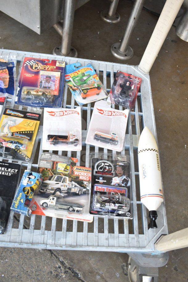 Assorted items including die-cast cars, Hot Wheels, and a NASA rocket model in original packaging. Various sizes and themes.