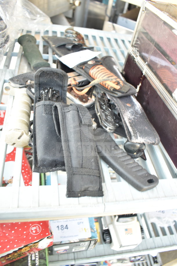 Assorted items including knives, knuckles, and drill bits with cases, on a shelf. Variety of handles and materials visible.