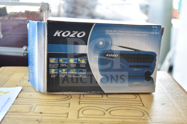 Boxed Kozo FM/AM World Band Receiver with flashlight, solar, and crank power features. Appears with Holy Bible book underneath.