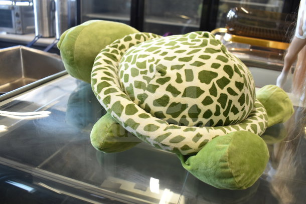 Green and white turtle stuffed animal with patterned shell, in good condition, displayed on glass surface.