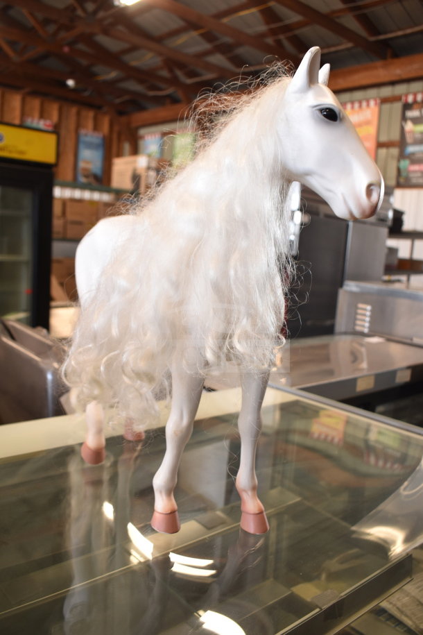 White play horse with long, curly white mane on a glass surface in a warehouse setting.