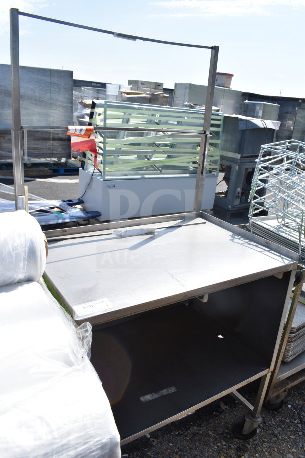 Commercial table with under shelf and casters. Steel construction, used condition. Item tag indicating auction number.