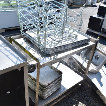 2 tier metal cart with wheels, holding metal baking pans and silver racks, in used condition outdoors.