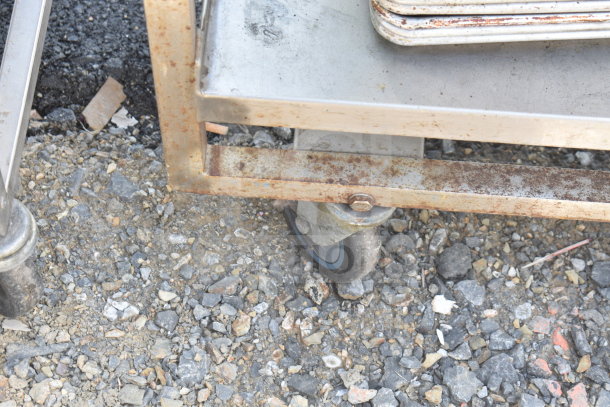 Rusty 2-tier metal cart with caster wheels, holding stacked baking pans. Visible wear and discoloration.