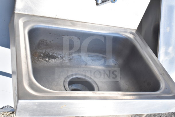 Commercial single bay wall mount sink with faucet and handles, visible wear. Made of stainless steel. Ideal for industrial use.
