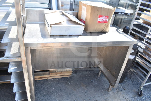 Stainless steel counter with shelving, used condition. Markings indicate "Fragile" on cardboard boxes on top.
